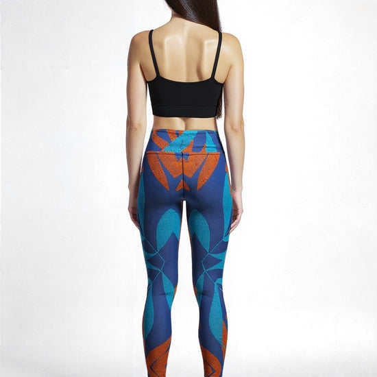 Back view of a model wearing Pixie & Sherbet’s Rustic Rhythm Yoga leggings featuring a bold geometric print in teal, orange, and blue tones, paired with a black crop top and black sneakers, set against a clean white background.