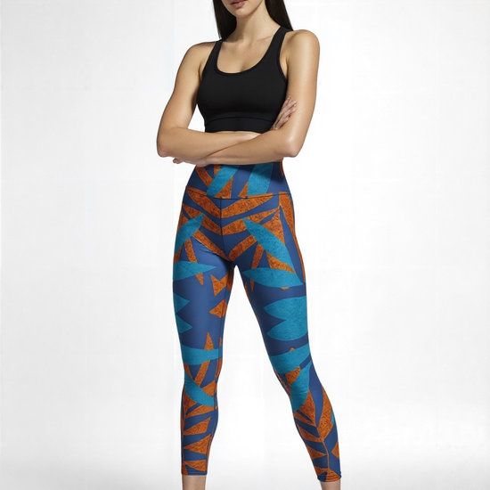 Front view of a model wearing Pixie & Sherbet’s Rustic Rhythm Yoga leggings with a bold blue and orange geometric print, styled with a black sleeveless crop top and black sneakers, posed confidently against a white backdrop