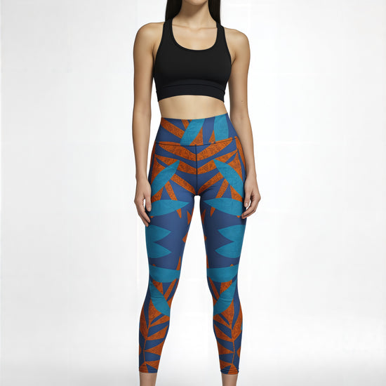 Model wearing Pixie & Sherbet’s Rustic Rhythm Yoga leggings with a vibrant blue and orange angular print, paired with a black sports bra and black sneakers, standing confidently against a white background