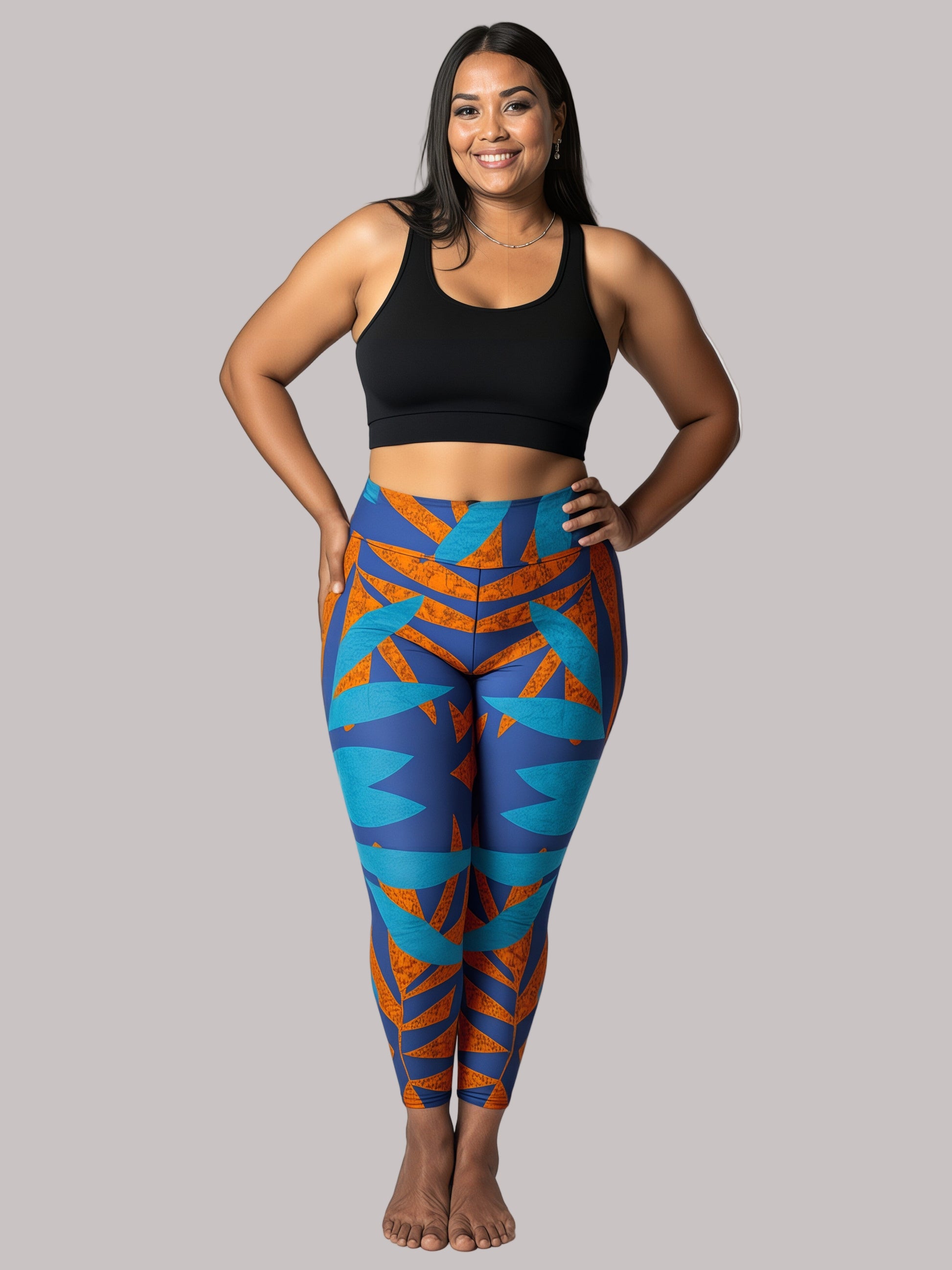 Model smiling in Pixie & Sherbet’s Rustic Rhythm Yoga leggings with bold blue and burnt orange geometric patterns, paired with a black sports bra, standing barefoot against a white background in a relaxed, confident pose