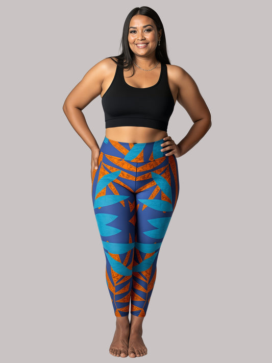 Model smiling in Pixie & Sherbet’s Rustic Rhythm Yoga leggings with bold blue and burnt orange geometric patterns, paired with a black sports bra, standing barefoot against a white background in a relaxed, confident pose