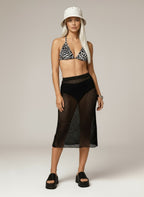 Woman wearing a black and white patterned bikini top with a black fishnet skirt on a neutral background