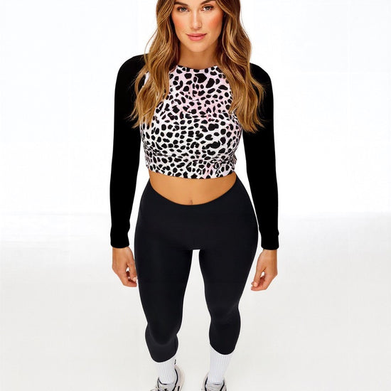 Front-facing view of model in Savannah Charge Surf Crop Top featuring black and white leopard print and solid black sleeves, styled with black leggings and white sneakers with pink accents; posed against white backdrop.