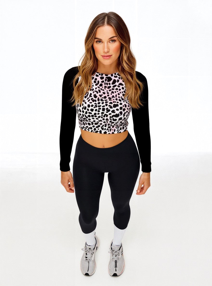 Front-facing view of model in Savannah Charge Surf Crop Top featuring black and white leopard print and solid black sleeves, styled with black leggings and white sneakers with pink accents; posed against white backdrop.