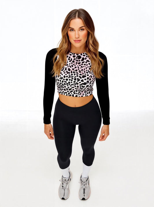 Front-facing view of model in Savannah Charge Surf Crop Top featuring black and white leopard print and solid black sleeves, styled with black leggings and white sneakers with pink accents; posed against white backdrop.