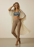 Woman wearing a leopard print top and beige leggings with a flowing beige garment against a plain background