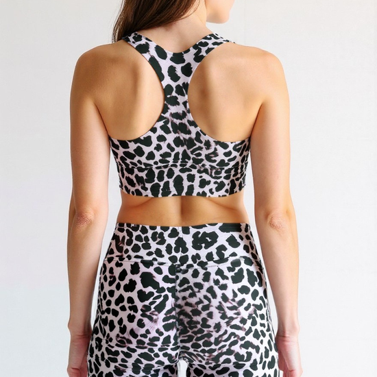 Back view of a woman wearing Savannah Charge yoga shorts and matching sports bra with a black and white cheetah print, showing the racerback design and high-waisted shorts.