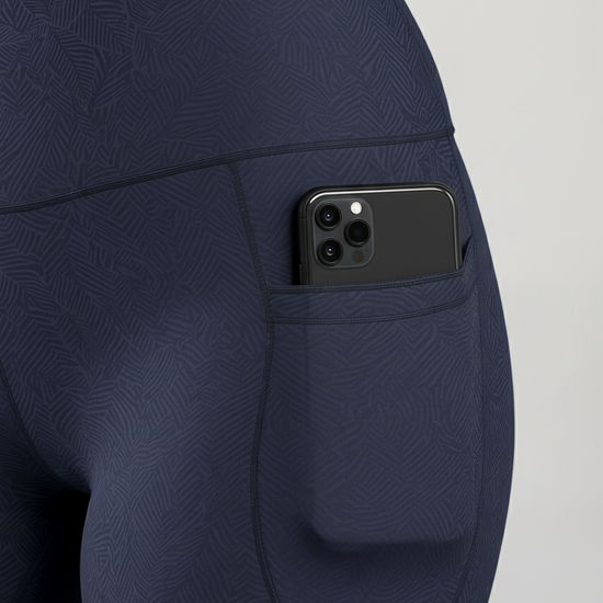 Navy blue leggings with a pocket holding a smartphone on a light gray background