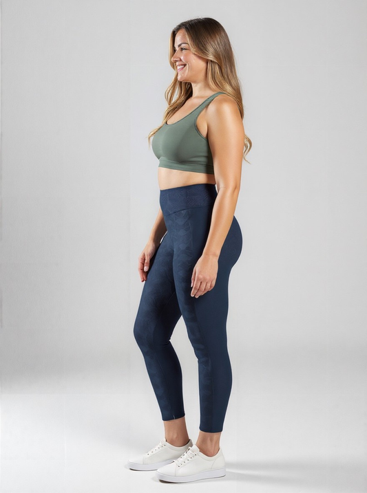 Smiling woman wearing navy blue high-waisted Shadowleaf Pocket Leggings and a sage green sports bra, standing in profile against a light grey background.