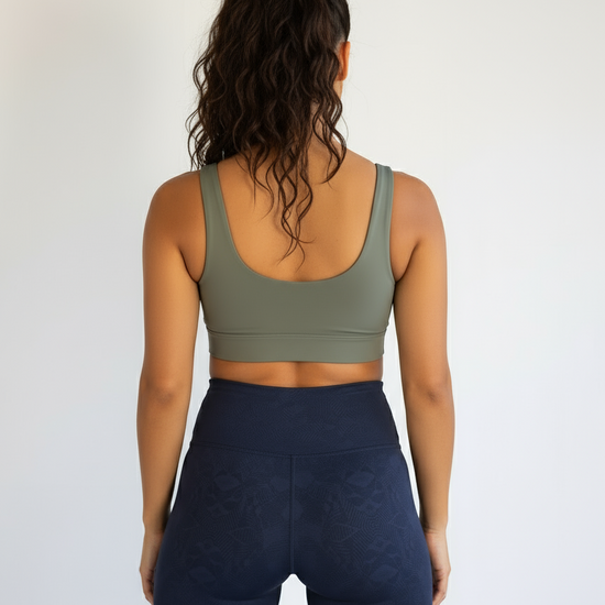 Person wearing an olive green sports bra and navy blue shorts on a plain background