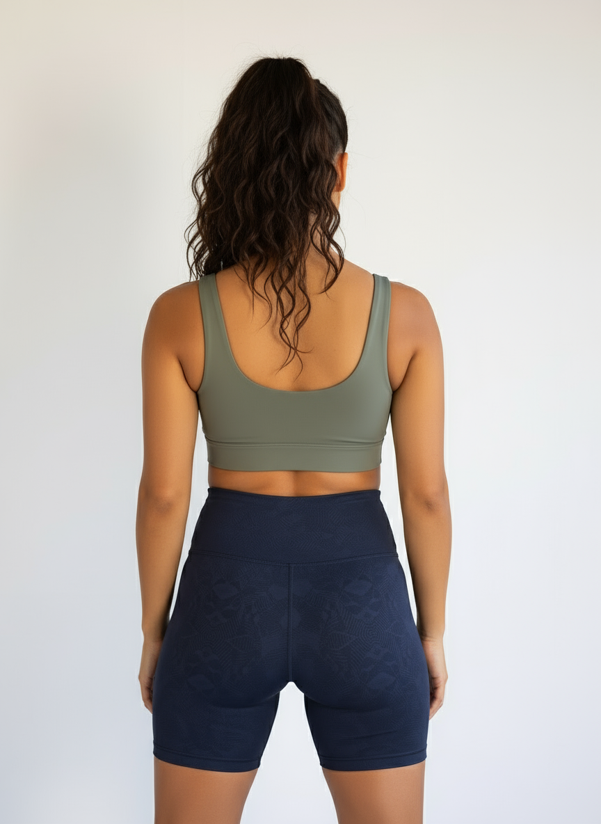 Person wearing an olive green sports bra and navy blue shorts on a plain background