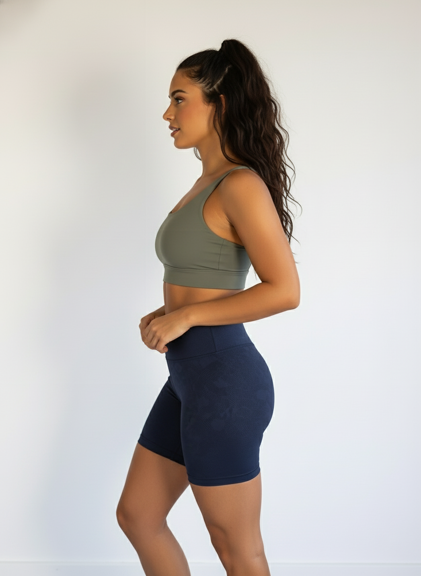 Woman wearing an olive green sports bra and navy blue shorts on a white background