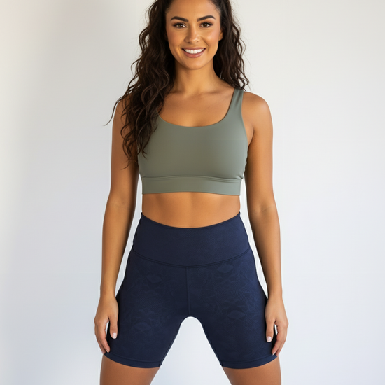 Woman wearing an olive green sports bra and navy shorts on a white background