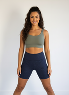 Woman wearing an olive green sports bra and navy shorts on a white background