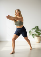 Woman in athletic wear practicing yoga in a bright room with large windows and plants.