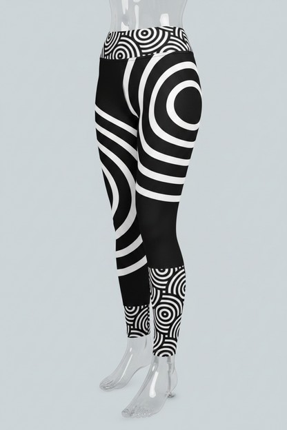 Black and white high-waisted leggings with a bold concentric spiral and circular optical illusion pattern, shown on a model against a solid light gray background.