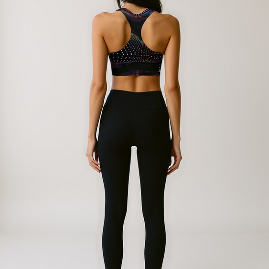 Back view of woman wearing Starlit Tempo longline sports bra with a black base and vibrant, multicolored starburst dot pattern, standing against a plain background