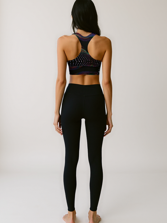 Back view of woman wearing Starlit Tempo longline sports bra with a black base and vibrant, multicolored starburst dot pattern, standing against a plain background