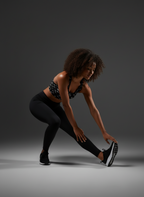 Woman in athletic wear stretching on a dark background
