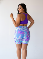 Woman wearing a purple sports bra and colorful patterned shorts on a white background