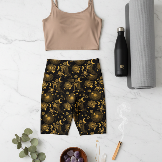 Beige tank top, black shorts with celestial pattern, black water bottle, gray yoga mat on a white marble surface.