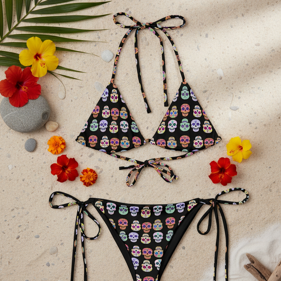 Colorful skull-patterned bikini set on a sandy background with flowers and leaves.