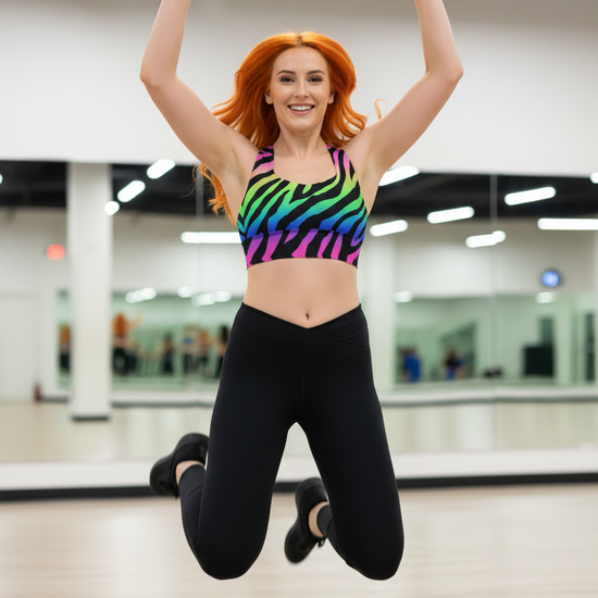 Person in a colorful sports bra and black leggings jumping in a gym.