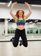 Person in a colorful sports bra and black leggings jumping in a gym.