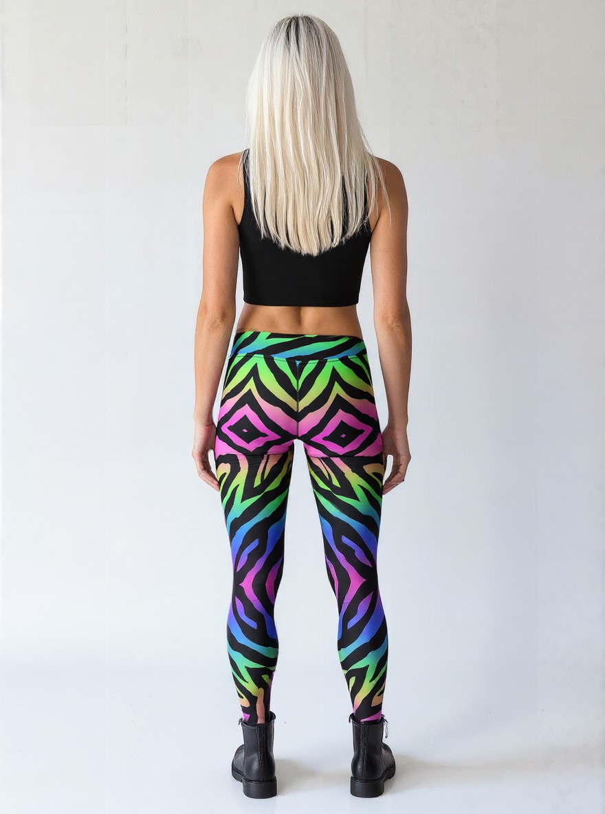 Athletic woman with long straight white hair and fair but tanned skin, shown from the back. She is wearing a black crop top, vibrant technicolour zebra-print yoga leggings, and black lace-up boots, standing against a plain light background.