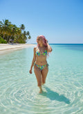 Woman in a colorful bikini standing in clear water with palm trees and blue sky in the background