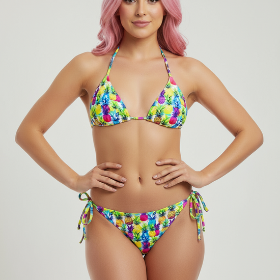 Model wearing Pixie & Sherbet ‘Tropic Like It’s Hot’ recycled string bikini with pineapple print, halter triangle top and tie‑side bottoms.