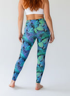 Person wearing blue tropical leaf pattern leggings on a white background