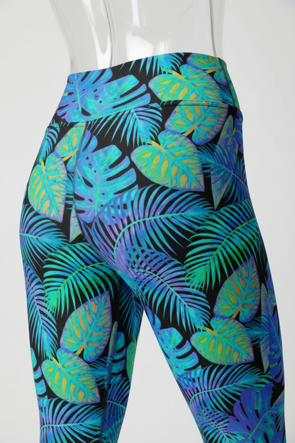 Close-up of a mannequin wearing high-waisted leggings with a bold tropical leaf print in bright blue, teal, green, and purple on a black background.