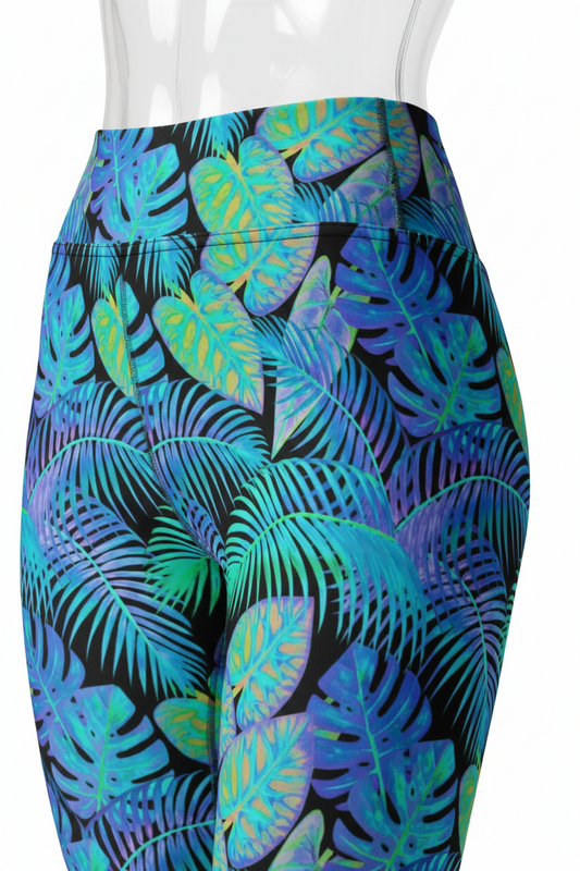Close-up of a mannequin wearing high-waisted athletic leggings with a bold tropical leaf print in blue, teal, green, and purple on a black background, paired with a beige sports bra.