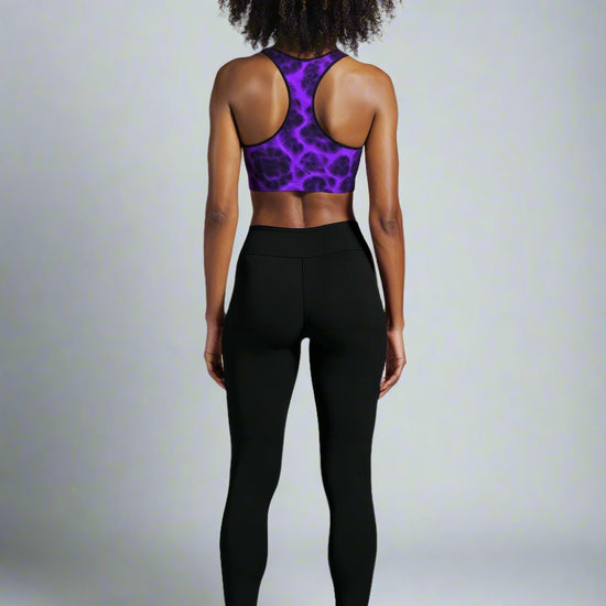 Back view of woman wearing Violet Voltage Essential Active Bra with a bold purple and black electric floral pattern, standing confidently against a plain background