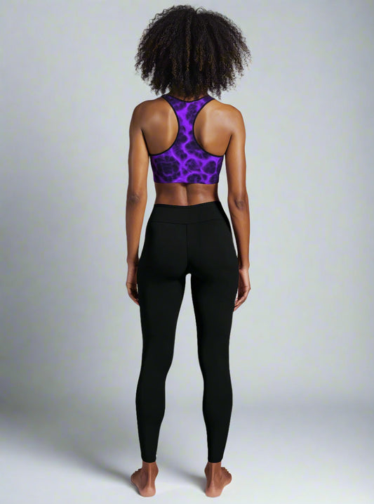 Back view of woman wearing Violet Voltage Essential Active Bra with a bold purple and black electric floral pattern, standing confidently against a plain background