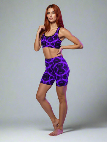 Woman wearing matching electric‑purple and black patterned sports bra and high‑waist shorts set, posing barefoot against a soft purple background — showcasing bold, luxe activewear style