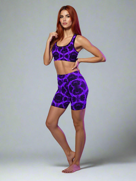 Woman wearing matching electric‑purple and black patterned sports bra and high‑waist shorts set, posing barefoot against a soft purple background — showcasing bold, luxe activewear style