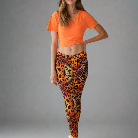 A woman is wearing Wildfire Crossover Leggings featuring a bold animal print pattern in vibrant orange, yellow, and black tones. The leggings have a flattering crossover waistband and a sleek, fitted silhouette. The design is eye-catching and inspired by wild cat prints, with the background kept simple to highlight the leggings' dynamic style.