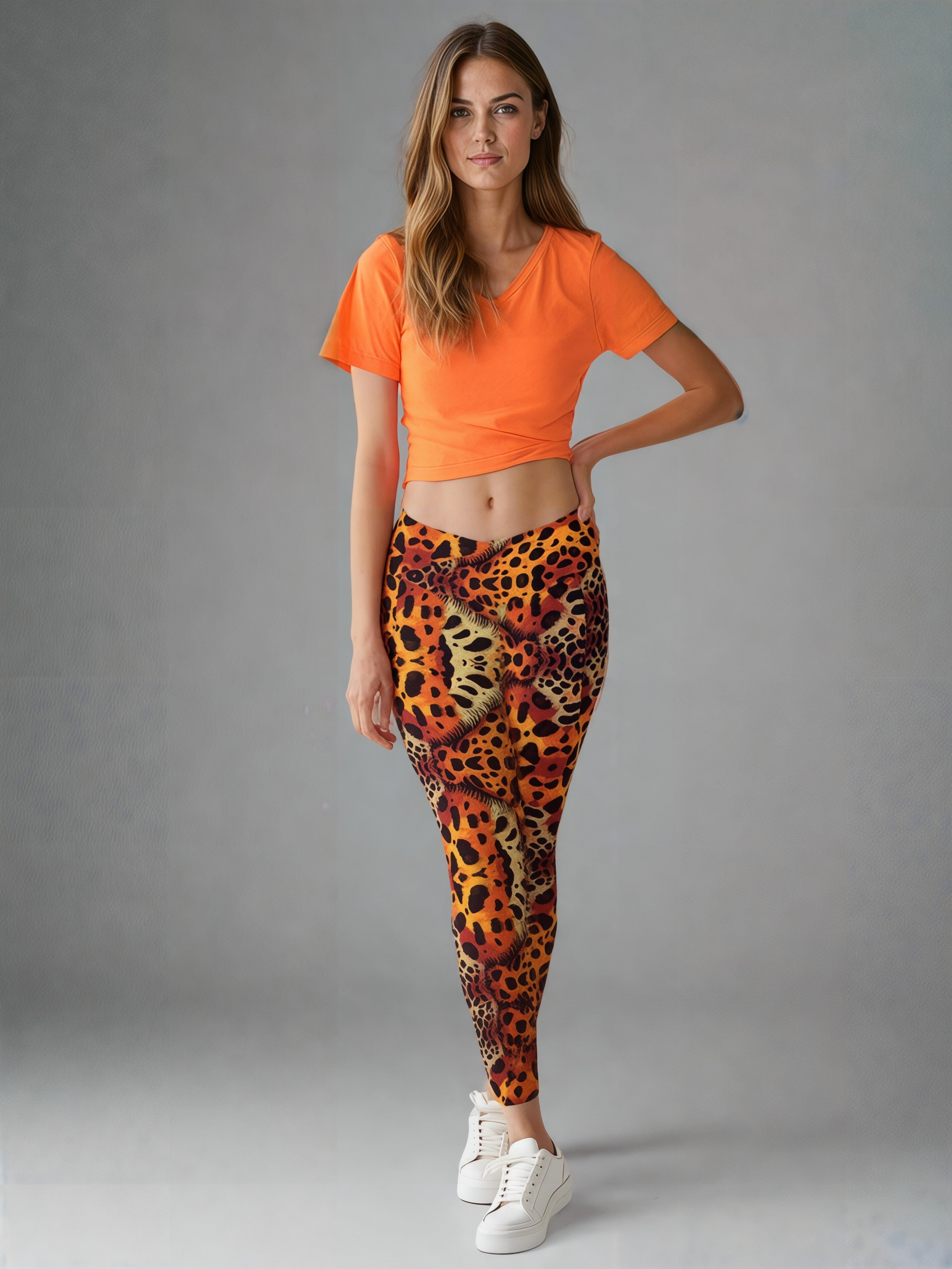 A woman is wearing Wildfire Crossover Leggings featuring a bold animal print pattern in vibrant orange, yellow, and black tones. The leggings have a flattering crossover waistband and a sleek, fitted silhouette. The design is eye-catching and inspired by wild cat prints, with the background kept simple to highlight the leggings' dynamic style.