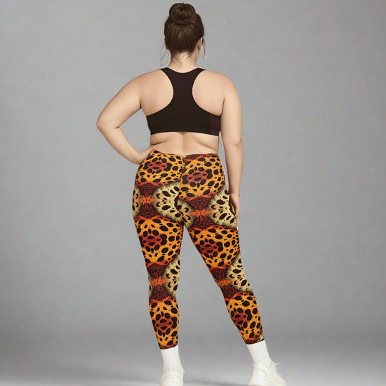 Back view of person wearing Wildfire Crossover Leggings with bold orange, red, and yellow animal print, paired with a black sports bra and white sneakers against a grey background.
