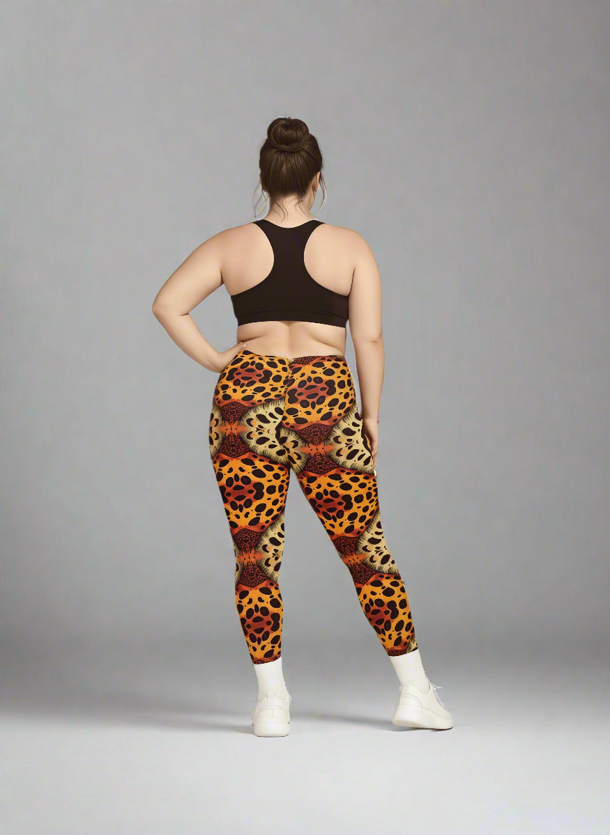 Back view of person wearing Wildfire Crossover Leggings with bold orange, red, and yellow animal print, paired with a black sports bra and white sneakers against a grey background.