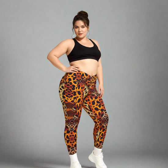 Women standing confidently in Wildfire Crossover Leggings with bold animal print in orange, red, and black, paired with a black sports bra and white sneakers against a plain grey backdrop.