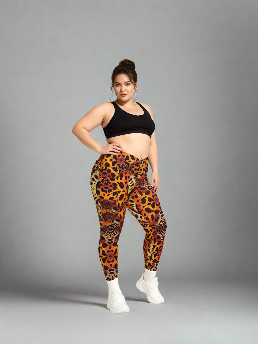 Women standing confidently in Wildfire Crossover Leggings with bold animal print in orange, red, and black, paired with a black sports bra and white sneakers against a plain grey backdrop.