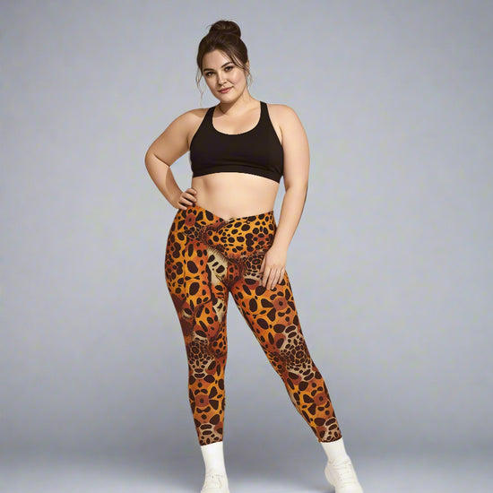 Person standing confidently in Wildfire Crossover Leggings with bold orange leopard print, paired with a black sports bra and white sneakers against a light grey background.