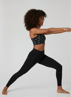 Woman in black athletic leggings and sports bra posing against a white background